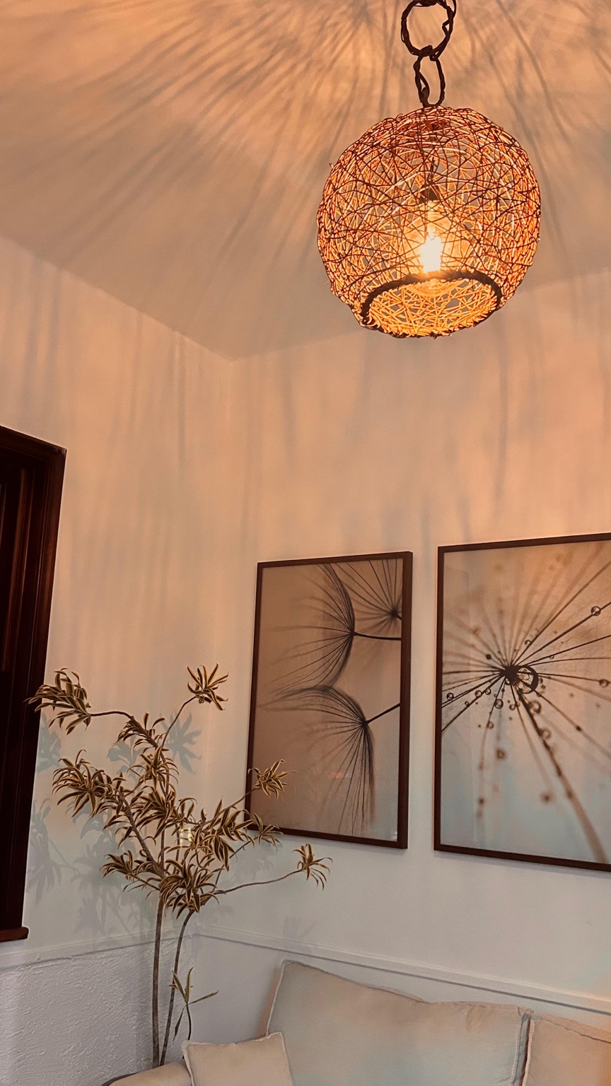 Nosso espaço: luz acolhedora de uma luminária de fibras, planta e quadros botânicos ao lado do sofá.